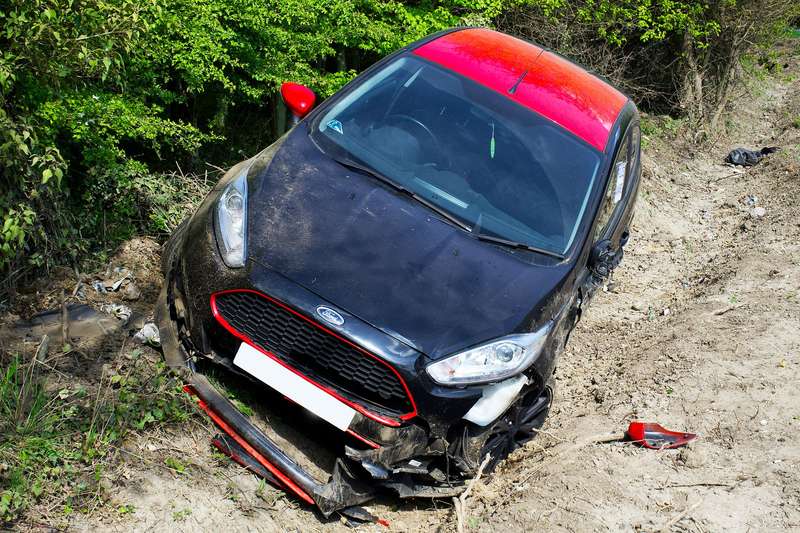 Schwarzes Auto mit zerstörter Front steht nach einem Unfall schräg im Straßengraben