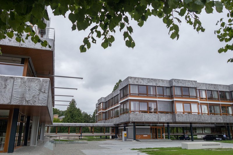 Flacher Gebäuderiegel des Bundesverfassungsgerichts in Karlsruhe, im Vordergrund Laub eines Baumes