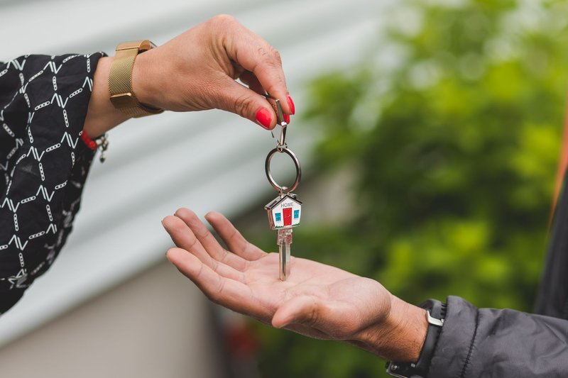 Eine Hand lässt einen Schlüssel mit Haus-Anhänger in die offene Handfläche einer anderen Person fallen