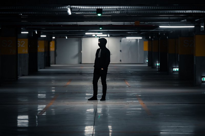 Dunkle Silhouette einer Person im Kapuzenpullover, die allein in einer schwach beleuchteten Tiefgarage steht
