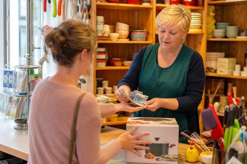 Verkäuferin zählt einer Kundin Geldscheine in die Hand, während diese den Karton zurückschiebt