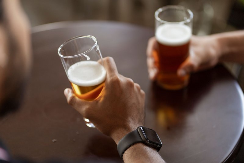 Zwei Hände halten Biergläser über einem runden Holztisch in einer Kneipe