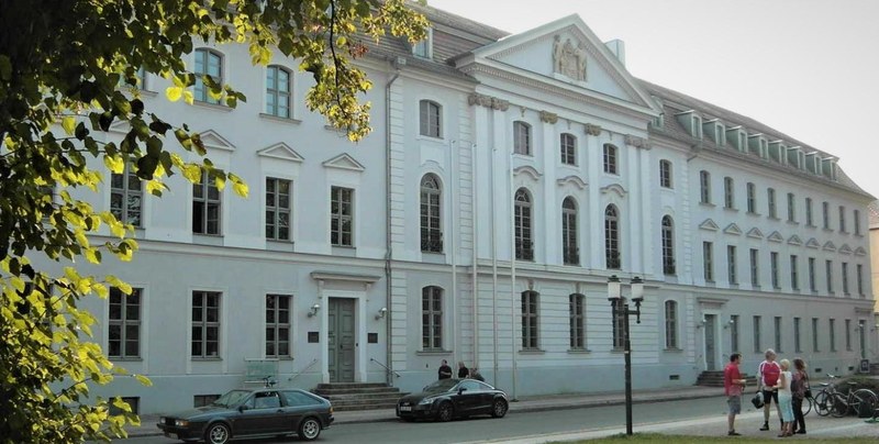 Klassizistische Fassade des Universitätshauptgebäudes Greifswald mit Mittelgiebel und langem Seitenflügel, Bäume im Vordergrund