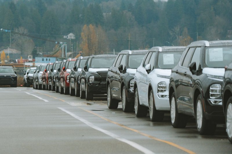 Lange Reihe geparkter Fahrzeuge auf dem Hof eines Autohauses an einem bewölkten Tag