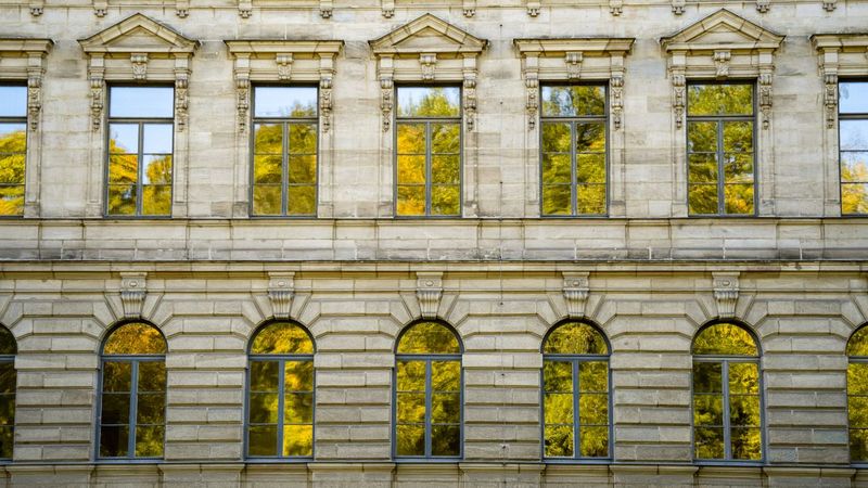 Historische Sandsteinfassade eines Gebäudes in Erlangen, in den Fenstern spiegelt sich herbstliches Laub