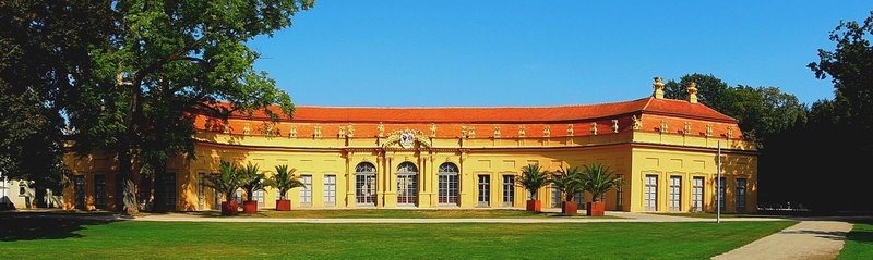 Die gelbe Orangerie im Erlanger Schlossgarten mit Rasenfläche und Kübelpflanzen davor
