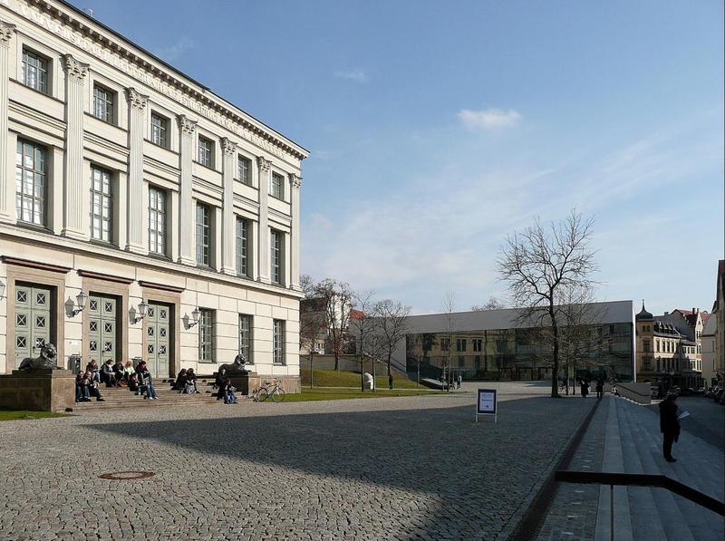 Löwengebäude der Martin-Luther-Universität am Universitätsplatz in Halle, davor sitzen Studierende auf den Stufen