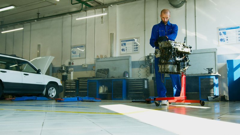 Kfz-Mechaniker hebt einen Austauschmotor an einem Motorkran in einer Werkstatt
