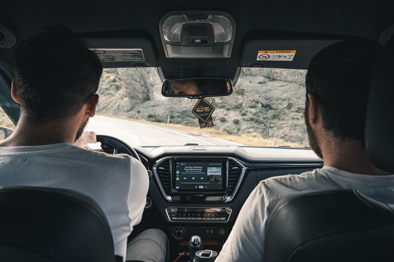 Blick von der Rückbank auf zwei Männer, die gemeinsam in einem Auto auf einer Landstraße unterwegs sind