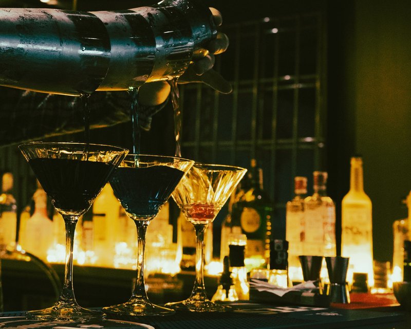 Barkeeper schenkt in einer abgedunkelten Bar mehrere Cocktailgläser gleichzeitig ein