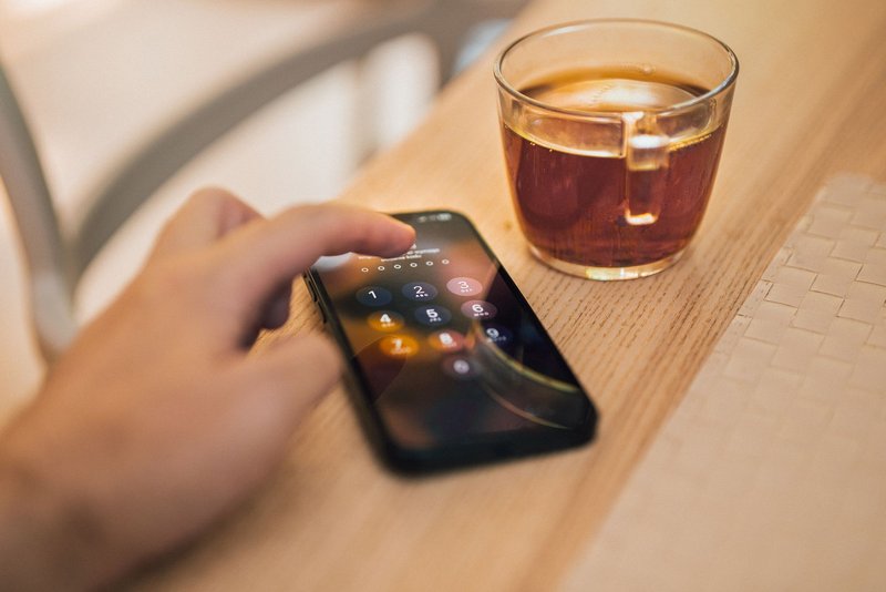 Hand tippt den Code auf einem Smartphone ein, daneben ein Glas Tee auf einer Holztheke