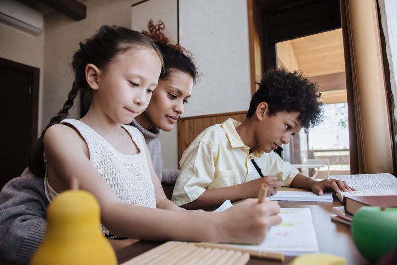 Mutter hilft ihren beiden Kindern am Tisch bei den Hausaufgaben