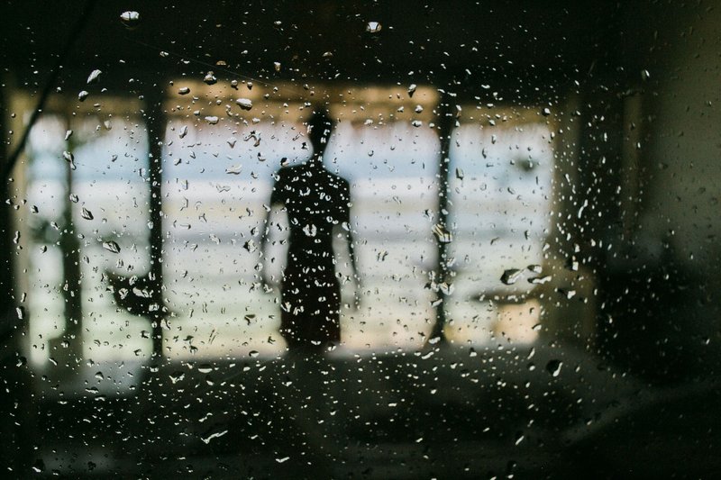 Silhouette einer Person hinter einer regennassen Fensterscheibe