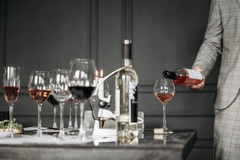Ein Sommelier schenkt Roséwein in ein Glas, daneben stehen weitere gefüllte Weingläser auf einem dunklen Tisch