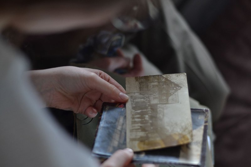 Eine Hand hält eine alte, vergilbte Fotografie über einem geöffneten Album