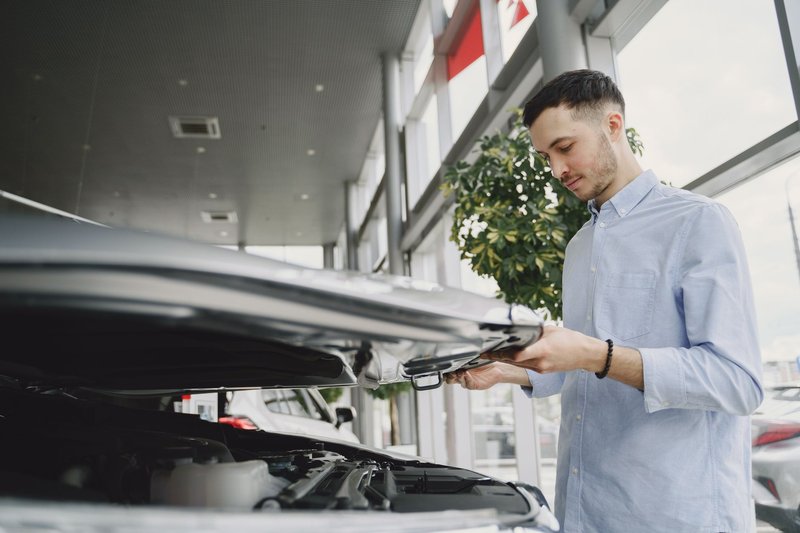 Ein Mann öffnet im Autohaus die Motorhaube eines Gebrauchtwagens und sieht in den Motorraum