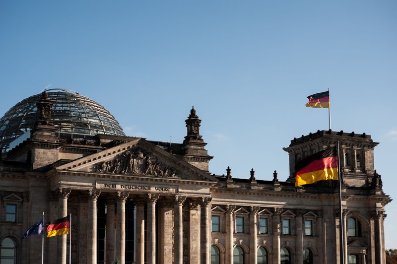 Reichstagsgebäude in Berlin mit Glaskuppel und wehenden Deutschlandflaggen vor blauem Himmel