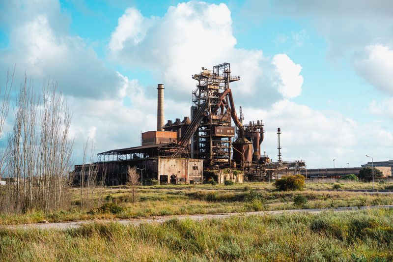 Verlassenes Hüttenwerk mit rostigem Hochofen und Schornstein hinter einer verwilderten Wiese