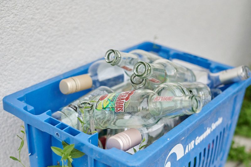 Eine blaue Getränkekiste mit leeren Glasflaschen steht vor einer hellen Hauswand
