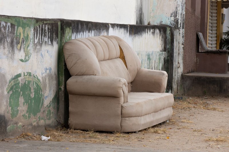 Ein ausrangiertes helles Sofa steht an einer verwitterten Hauswand am Straßenrand