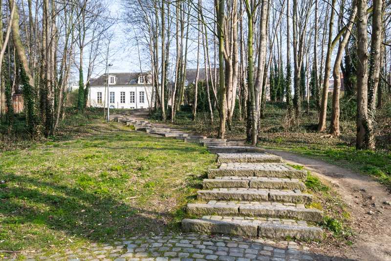 Steinerne Treppenstufen führen über einen Hang zu einem weiß verputzten Haus zwischen kahlen Bäumen