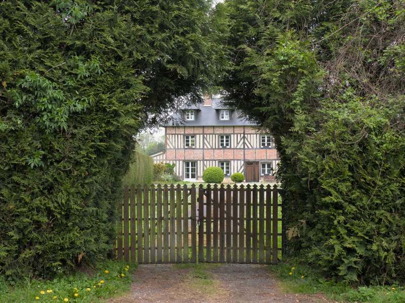 Geschlossenes Holztor auf einem Zufahrtsweg, dahinter ein Fachwerkhaus hinter hohen Hecken