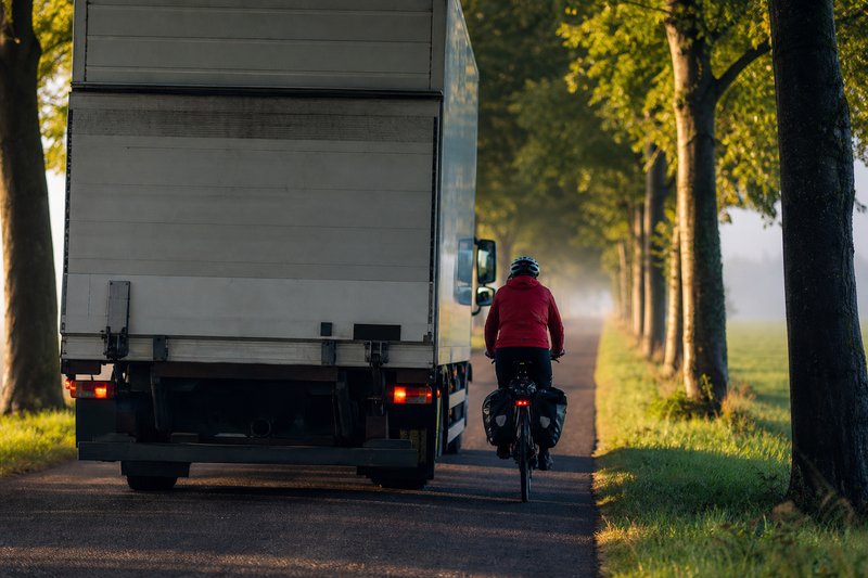 Lastwagen überholt einen Radfahrer auf einer schmalen Allee mit sehr geringem Seitenabstand