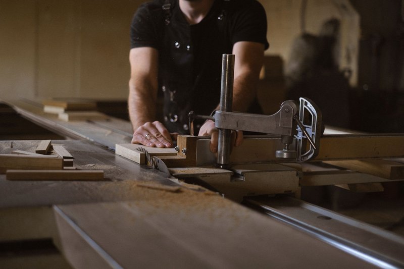 Tischler in Schürze bearbeitet an der Werkbank ein eingespanntes Holzbrett