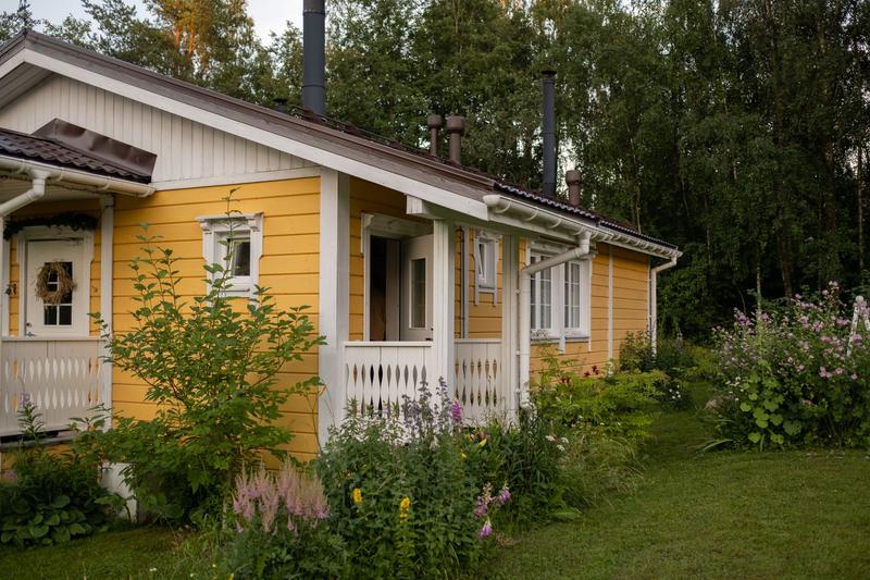 Gelbes Holzferienhaus mit weißer Veranda und blühendem Garten im Sommer