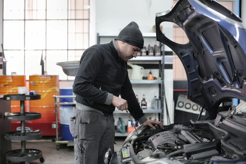 Mechaniker prüft in einer Werkstatt den Ölstand unter der geöffneten Motorhaube eines Autos