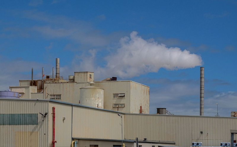 Industrieanlage mit rauchendem Schornstein unter blauem Himmel