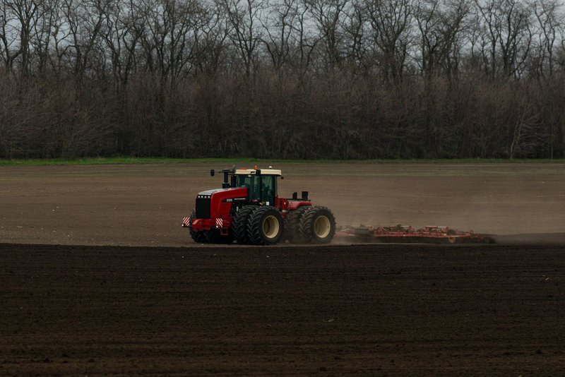 Roter Traktor zieht eine Egge über einen frisch bearbeiteten Acker