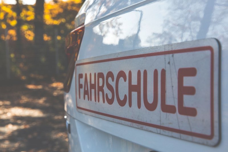 Weißes Auto mit rotem Fahrschule-Schild am Heck vor herbstlich gefärbten Bäumen