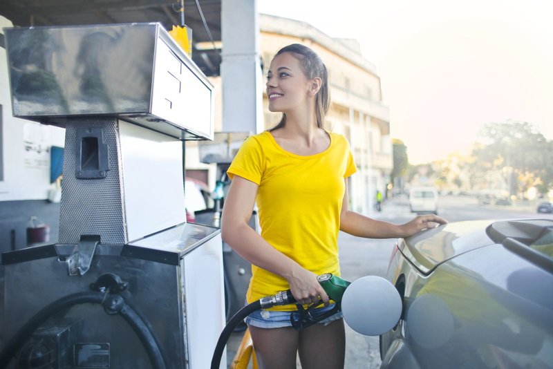 Junge Frau im gelben T-Shirt tankt ein Auto an einer Zapfsäule