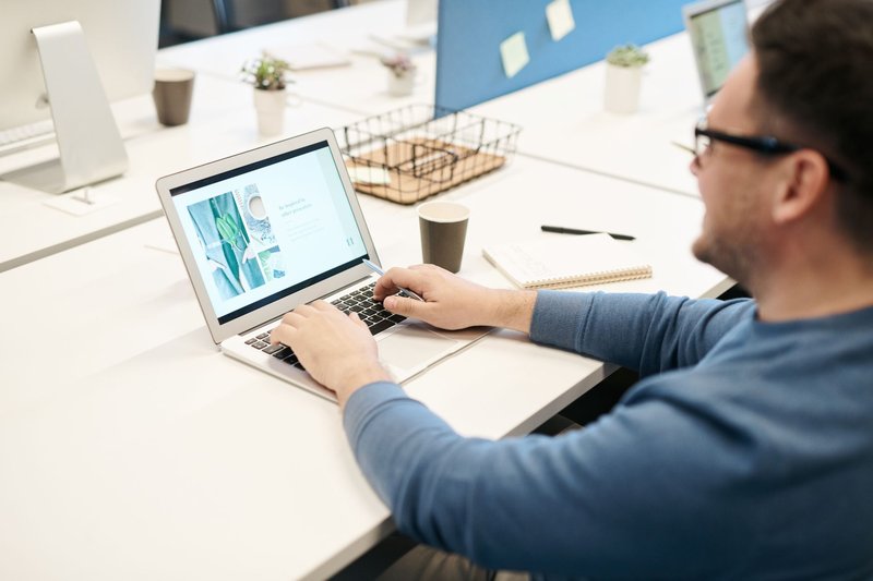 Mann mit Brille sitzt am Schreibtisch, tippt auf seinem Laptop und blickt auf den Bildschirm
