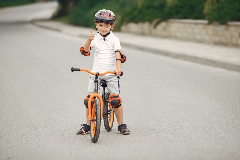 Junge mit Helm steht mit einem orangefarbenen Fahrrad auf der Straße