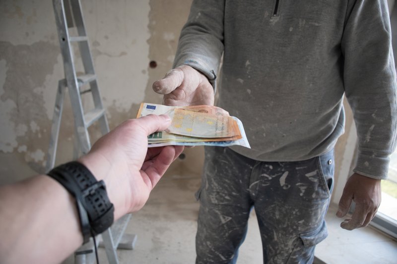 Hand reicht Euroscheine an einen Handwerker in einem unverputzten Raum