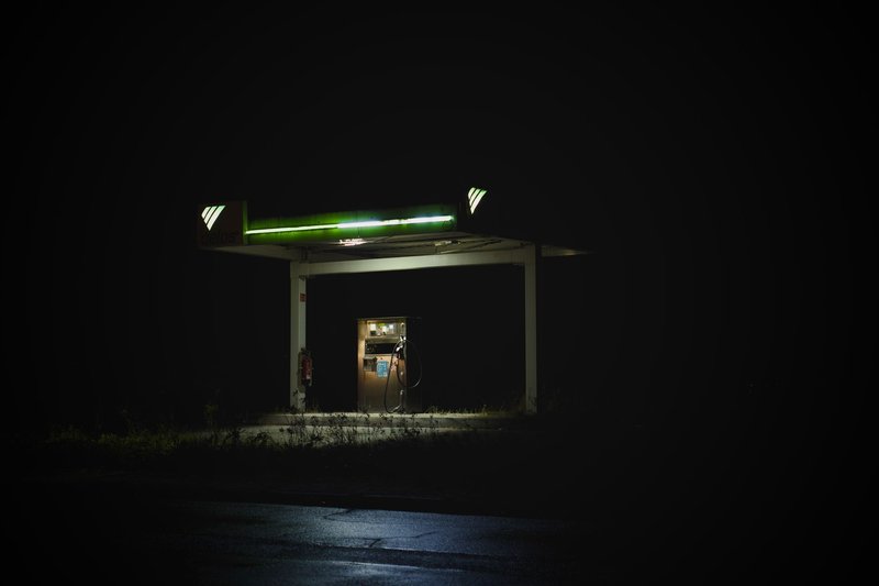 Beleuchtete Tankstelle bei Nacht, von der Straße aus gesehen, niemand am Kassenbereich