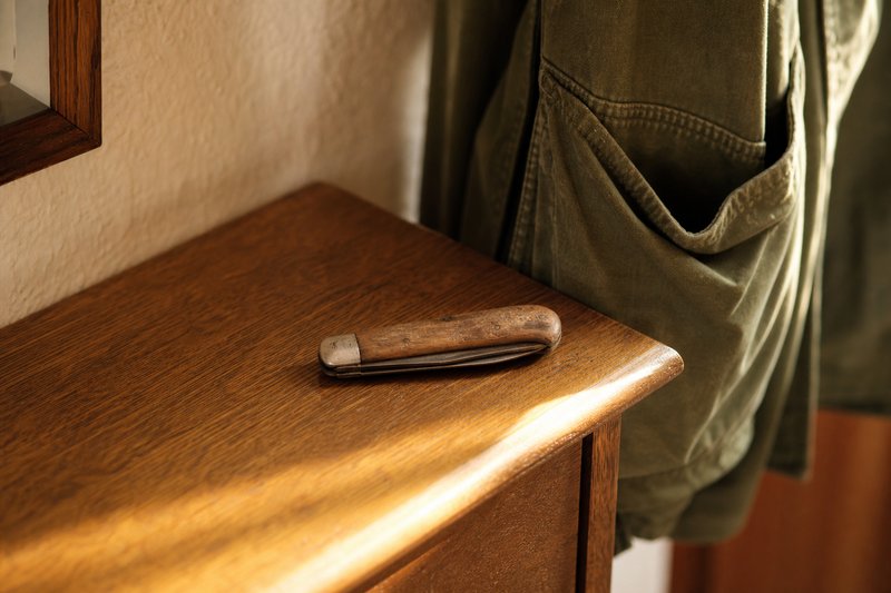 Geschlossenes Taschenmesser auf einer Flurkommode, daneben hängt eine olivgrüne Jacke
