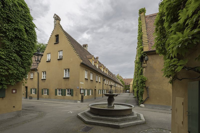 Gasse mit Brunnen und gelben Häuserzeilen in der Augsburger Fuggerei