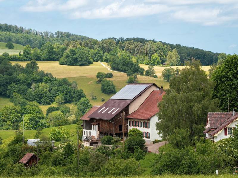 Bauernhof mit Scheune und Solarmodulen auf dem Dach inmitten grüner Hügel und Wälder