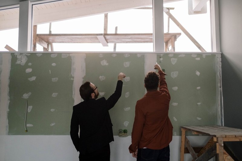 Zwei Männer zeigen bei einer Begehung im Rohbau auf Stellen einer gespachtelten Trockenbauwand