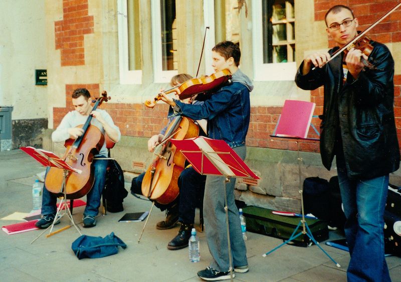 Streichquartett aus vier Musikern mit zwei Geigen und zwei Celli spielt vor einer Backsteinfassade