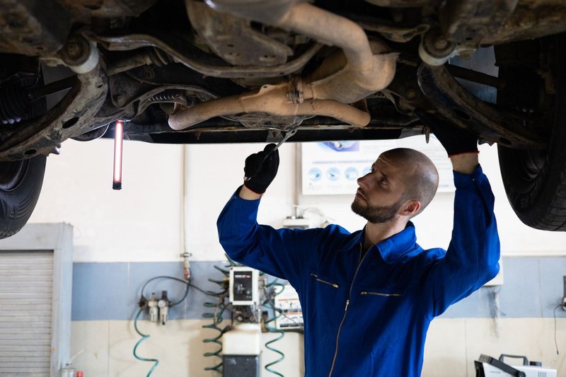 Mechaniker im blauen Overall arbeitet unter einem Auto auf der Hebebühne an der Abgasanlage