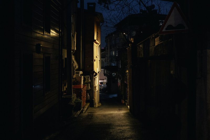 Dunkle, menschenleere Gasse bei Nacht, eine Lampe wirft warmes Licht auf das Pflaster.