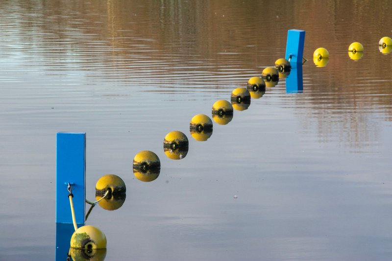 Absperrleine mit gelben Bojen und blauen Pfosten auf einem ruhigen See