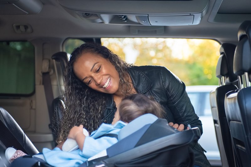 Frau beugt sich im Auto über ein Baby, das in einer Babyschale auf der Rückbank sitzt