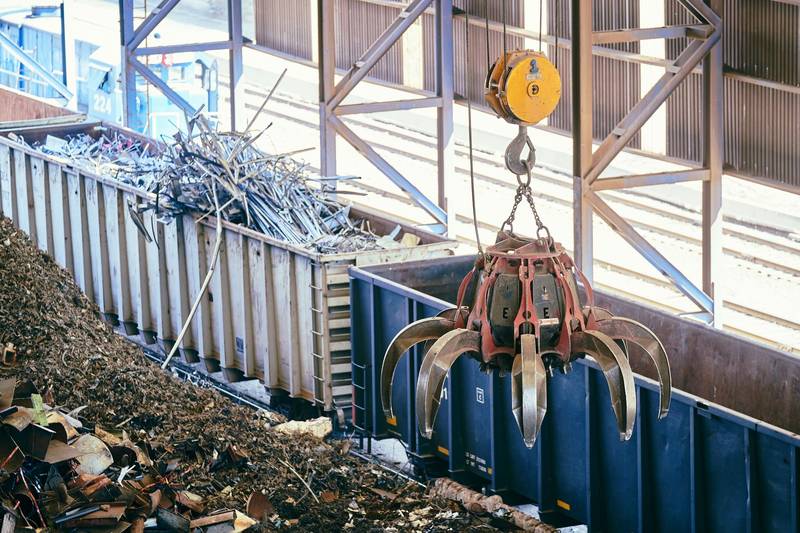 Greifer einer Kranbahn sortiert Metallschrott über Containern in einer Recyclinganlage