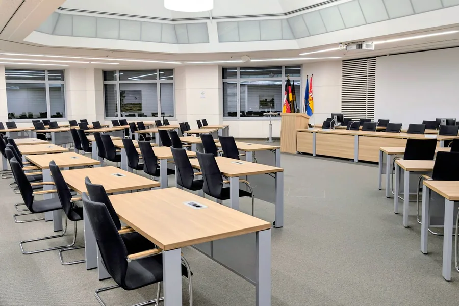 Leerer Plenarsaal eines deutschen Landesparlaments mit Stuhlreihen und Landesflagge