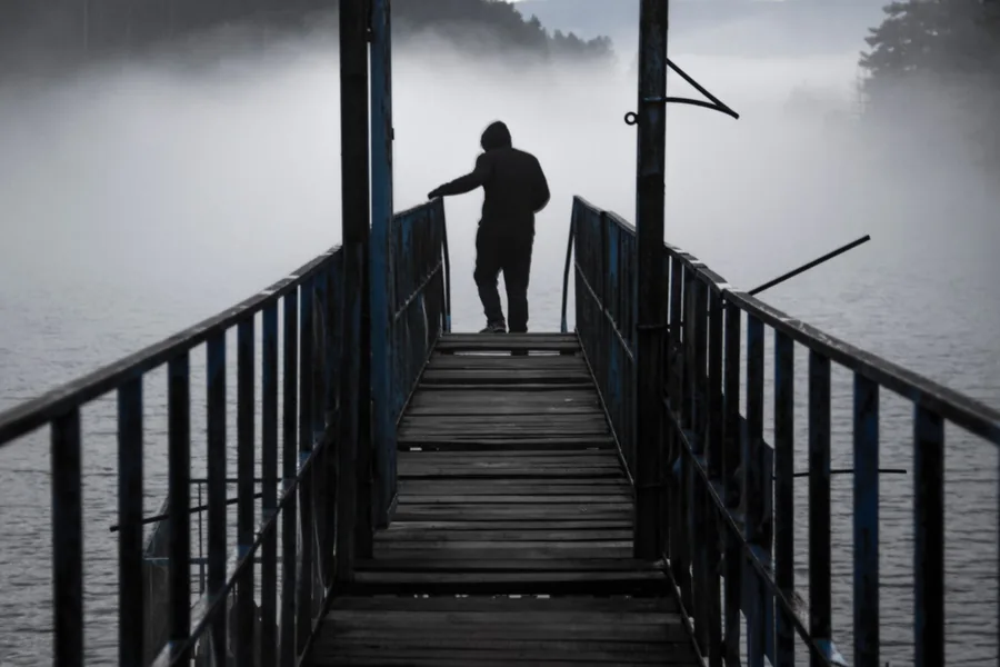 Eine Person steht auf einem Steg und blickt auf einen dunklen See im Nebel